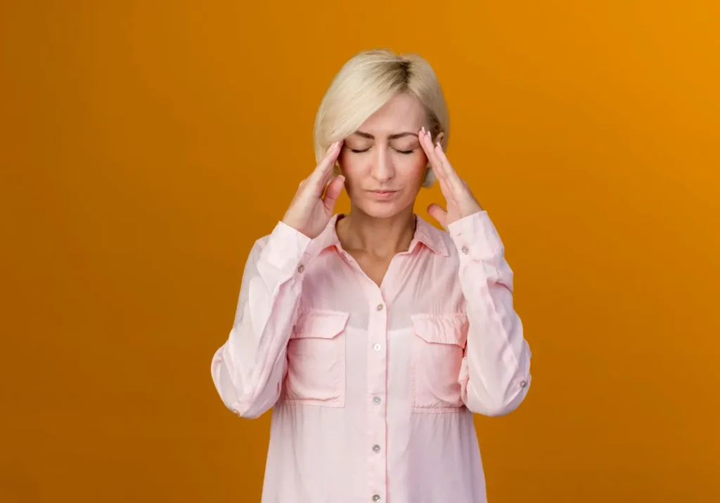 mulher com as mãos na cabeça indicando dor, um do sintomas iniciais do tumor cerebral
